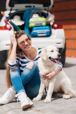 Woman with dog by car full of suitcases.