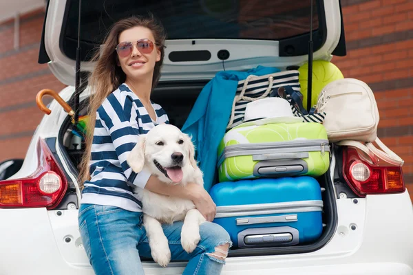 Woman with dog by car full of suitcases. — ストック写真