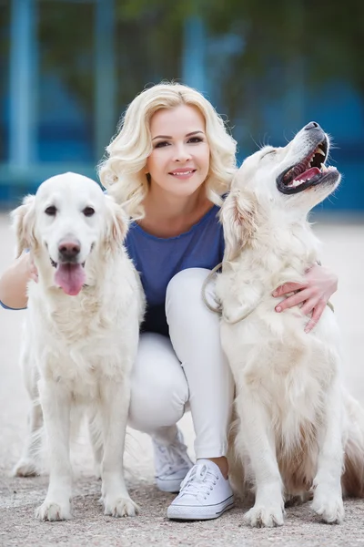 Femme blonde avec deux récupérateurs labrador doré en plein air . — Photo