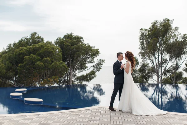 La novia y el novio junto a la piscina con agua azul — Foto de Stock