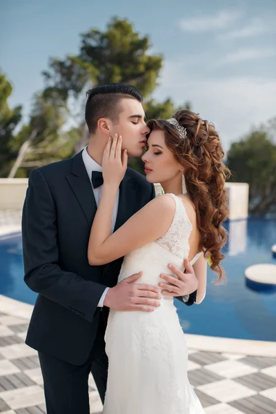 La novia y el novio junto a la piscina con agua azul — Foto de Stock