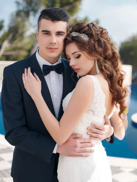 La novia y el novio junto a la piscina con agua azul — Foto de Stock