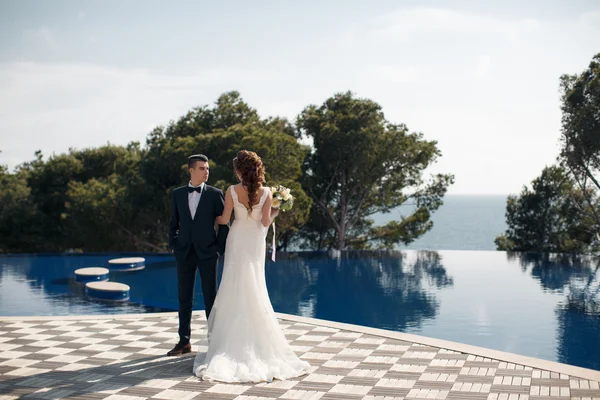 La novia y el novio junto a la piscina con agua azul —  Fotos de Stock