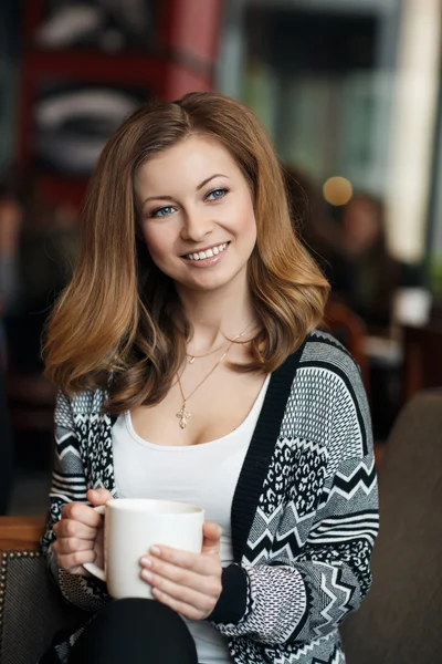 Bela jovem mulher sorridente com uma xícara de café em um café — Fotografia de Stock