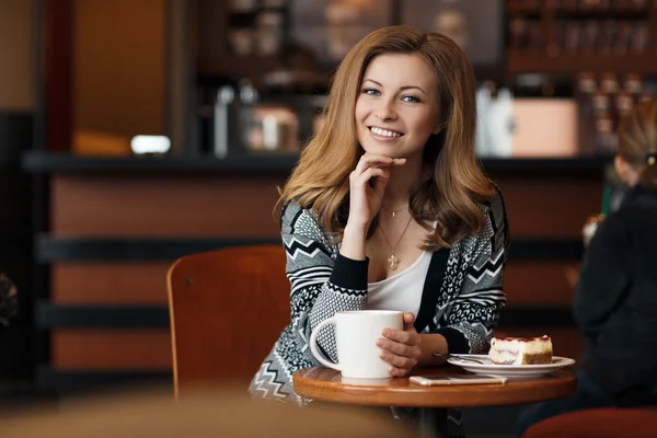 Όμορφη νεαρή χαμογελαστή γυναίκα με ένα φλιτζάνι καφέ σε μια καφετέρια — Φωτογραφία Αρχείου