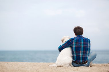 Yaz sahilinde köpeğiyle birlikte kameraya geri oturan adam