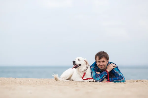 Retrato de primavera de um jovem com um cachorro na praia — Fotografia de Stock