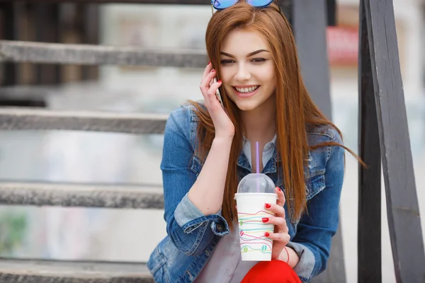 Egy fiatal nő, kezében egy koktél, és a telefonhívást a mobiltelefonján — Stock Fotó