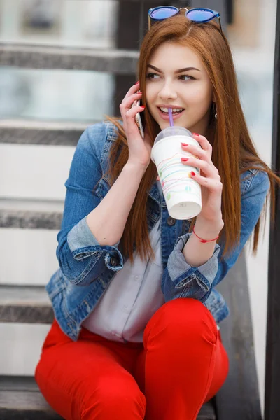 Uma jovem, segurando um coquetel e fazendo um telefonema em um telefone celular — Fotografia de Stock