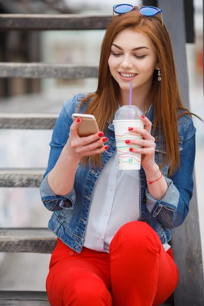 Mujer joven con un cóctel, leyendo un mensaje de texto en la calle — Foto de Stock