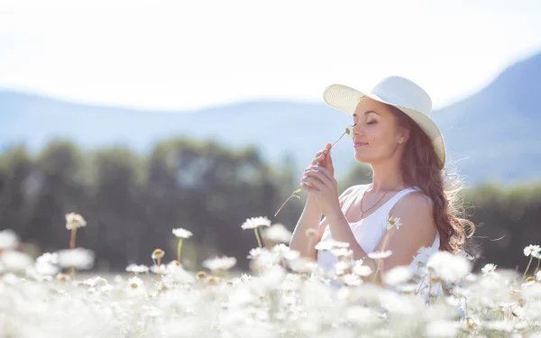 Portret van een jonge vrouw die een hoed draagt op een veld van bloeiende madeliefjes — Stockfoto