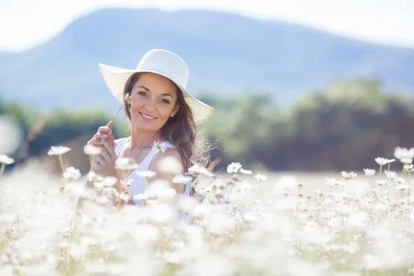 Retrato de uma jovem mulher usando um chapéu em um campo de margaridas florescendo — Fotografia de Stock