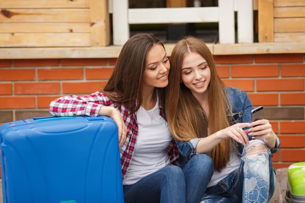 Două fete cu pungi care citesc mesaje text în timp ce stau la gară — Fotografie, imagine de stoc