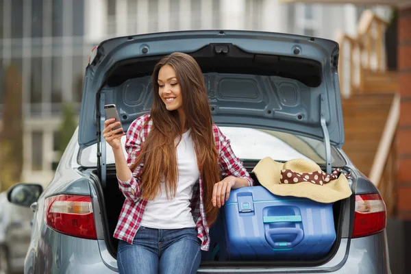 Young woman sitting in the car trunk with suitcases — Stock fotografie
