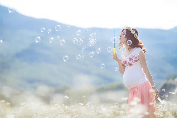 Portrait of beautiful pregnant woman in field blowing bubbles — Stock Photo, Image