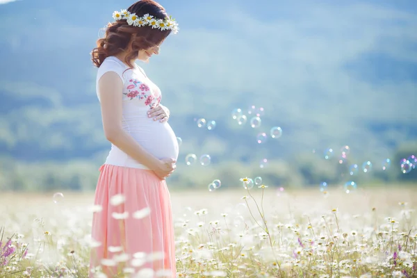 Portrait of beautiful pregnant woman in field blowing bubbles — Stock Photo, Image