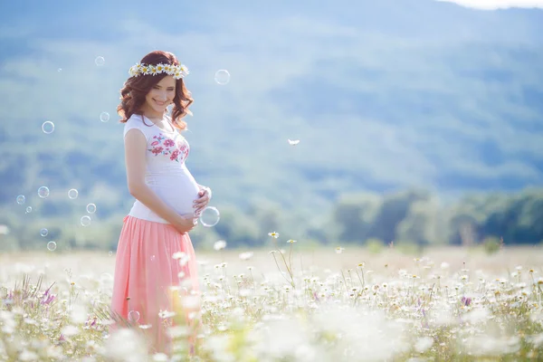 Portrait of beautiful pregnant woman in field blowing bubbles — Stock Photo, Image