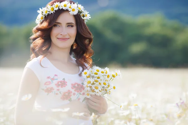 A pregnant woman in a field with a bouquet of white daisies — Stock Photo, Image