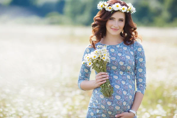 Pregnant woman in field with bunch of daisies — Stock Photo, Image