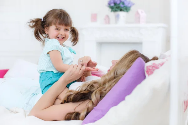 Jovem mãe feliz brincando com sua filha na cama em casa . — Fotografia de Stock