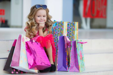 Cute little girl with colorful bags for shopping in supermarket clipart