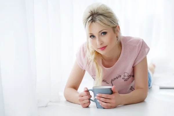 Belle femme couchée sur un sol blanc avec une tasse de thé — Photo