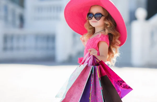 Linda niña en sombrero de moda con bolsas de compras al lado de un supermercado — Foto de Stock