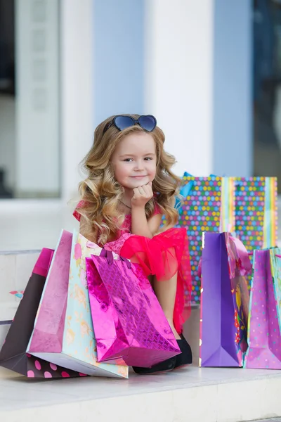 Söt liten flicka med färgglada väskor för shopping i stormarknad — Stockfoto