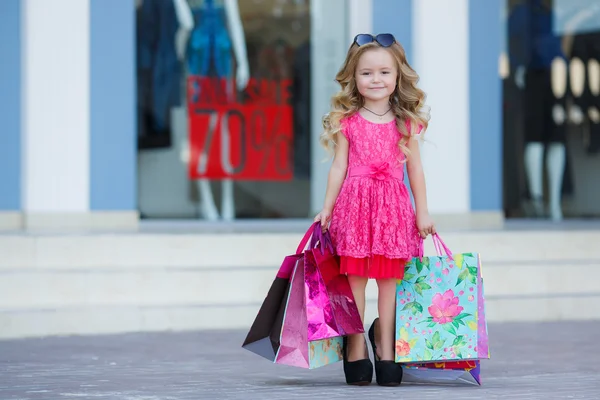 Söt liten flicka med färgglada väskor för shopping i stormarknad — Stockfoto