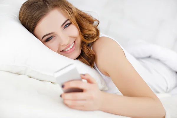 Gadis berambut merah membaca pesan di smartphone saat berbaring di tempat tidur — Stok Foto