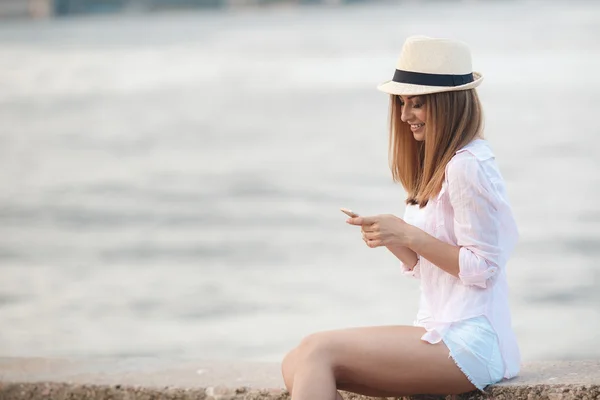 Brunett tjej avkopplande på stranden med telefonen — Stockfoto