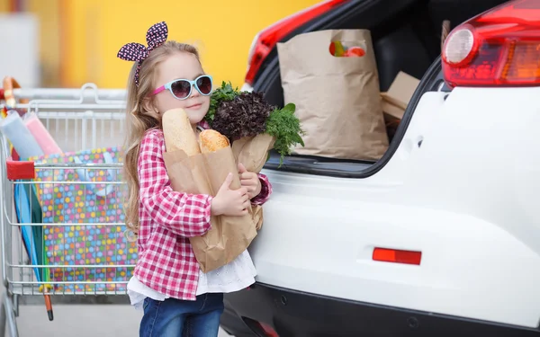 Mädchen mit Einkaufswagen voller Lebensmittel in der Nähe des Autos — Stockfoto