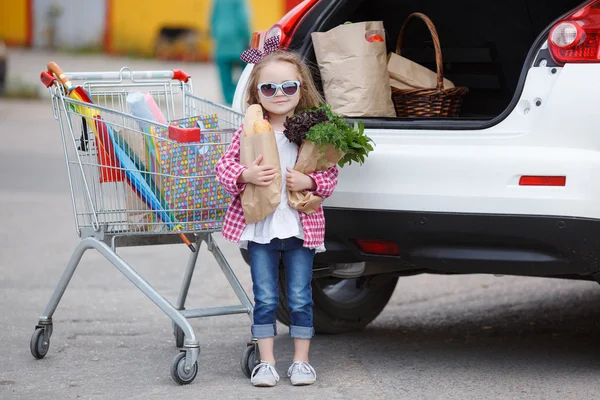 Девушка с тележкой, полной продуктов возле машины — стоковое фото