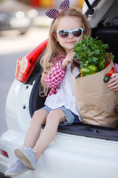Küçük kız-ürünlerin alıcı, bir arabanın açık bagajında oturan — Stok fotoğraf