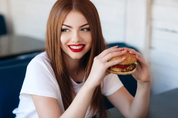 Lady with a hamburger for a table in a cafe — Stock Photo, Image