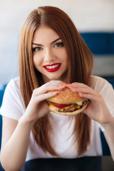 Lady with a hamburger for a table in a cafe
