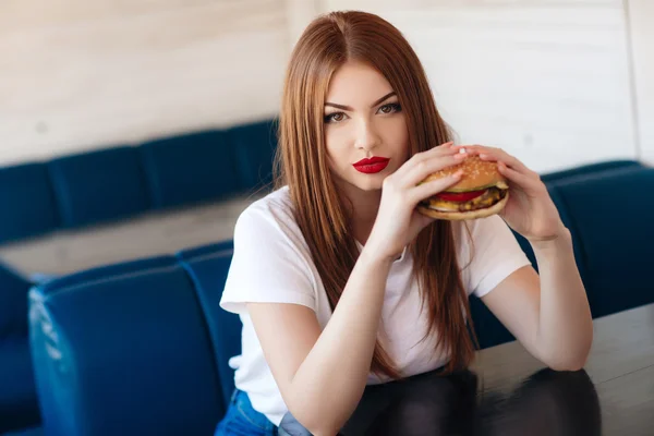 Dame mit einem Hamburger für einen Tisch in einem Café — Stockfoto