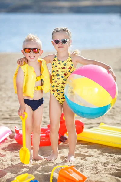 Menino e menina em uma praia de areia com uma grande bola inflável — Fotografia de Stock