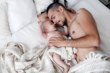 Bebekli bir adam. Evde mutlu bir aile. Mutlu bir baba ve iki aylık tatlı bir bebek evde hafif bir yatakta yatıyor.