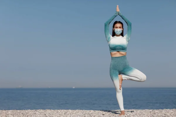 Молодая женщина в маске практикует йогу на открытом воздухе — стоковое фото