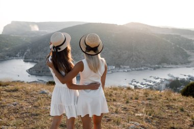 İki arkadaş, açık hava manzarası, deniz kenarında elbise ve şapka giymiş kızlar.
