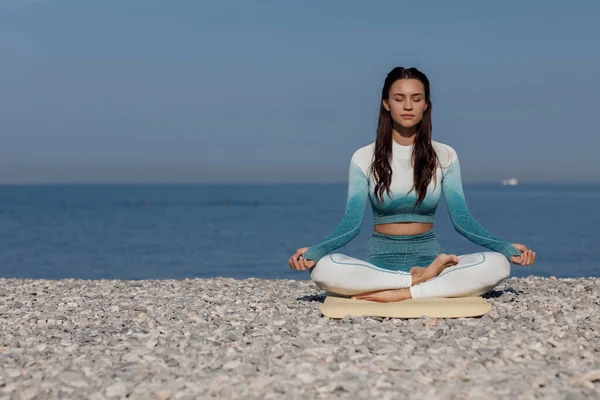 Kafkasyalı genç kadın deniz kıyısında yoga yapıyor. — Stok fotoğraf