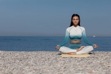 Kafkasyalı genç kadın deniz kıyısında yoga yapıyor.