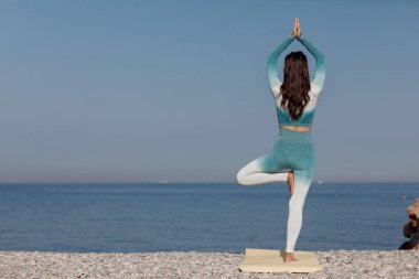 Kafkasyalı genç kadın deniz kıyısında yoga yapıyor.
