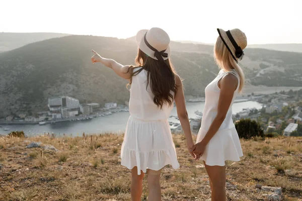 2つの幸せな友人、観光コンセプト夏休み。ドレスと帽子の親友。手によって道を示す — ストック写真