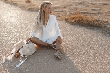 Açık havada şapka ve çanta taşıyan mutlu bir genç kadının portresi.