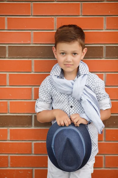 Snygg pojke i hatt poserar på en tegelvägg — Stockfoto