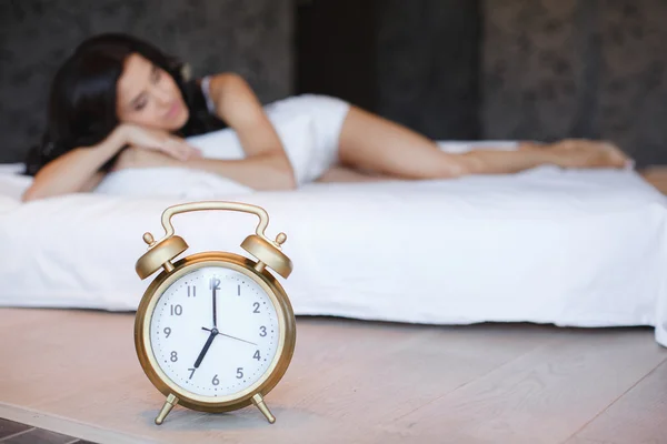 Uma jovem mulher com um despertador na cama pela manhã — Fotografia de Stock