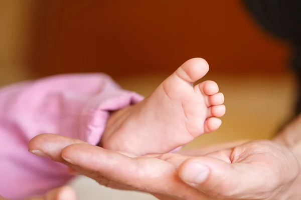 Les jambes du nouveau-né dans les mains douces de la mère — Photo