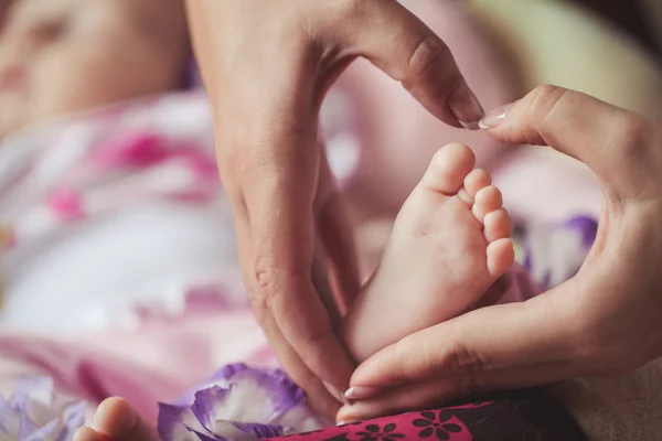 Les jambes du nouveau-né dans les mains douces de la mère — Photo